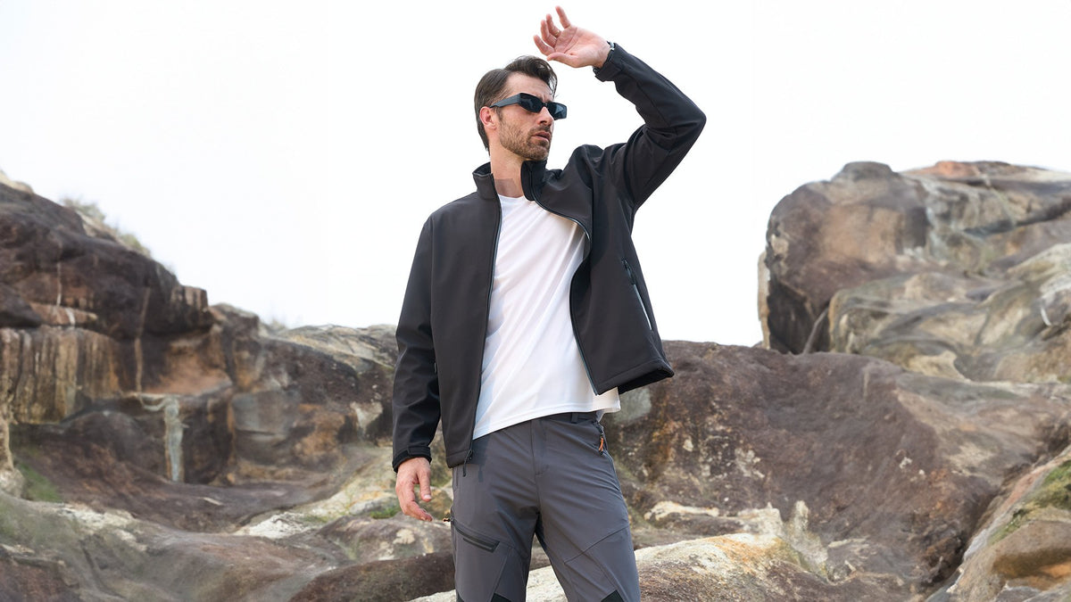 Man wearing a black MAGCOMSEN softshell jacket in a rocky outdoor setting